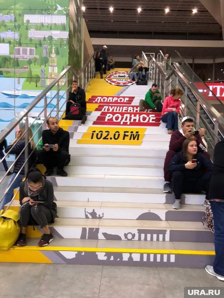 Пассажирам не хватает скамеек, люди сидят на ступеньках лестницы